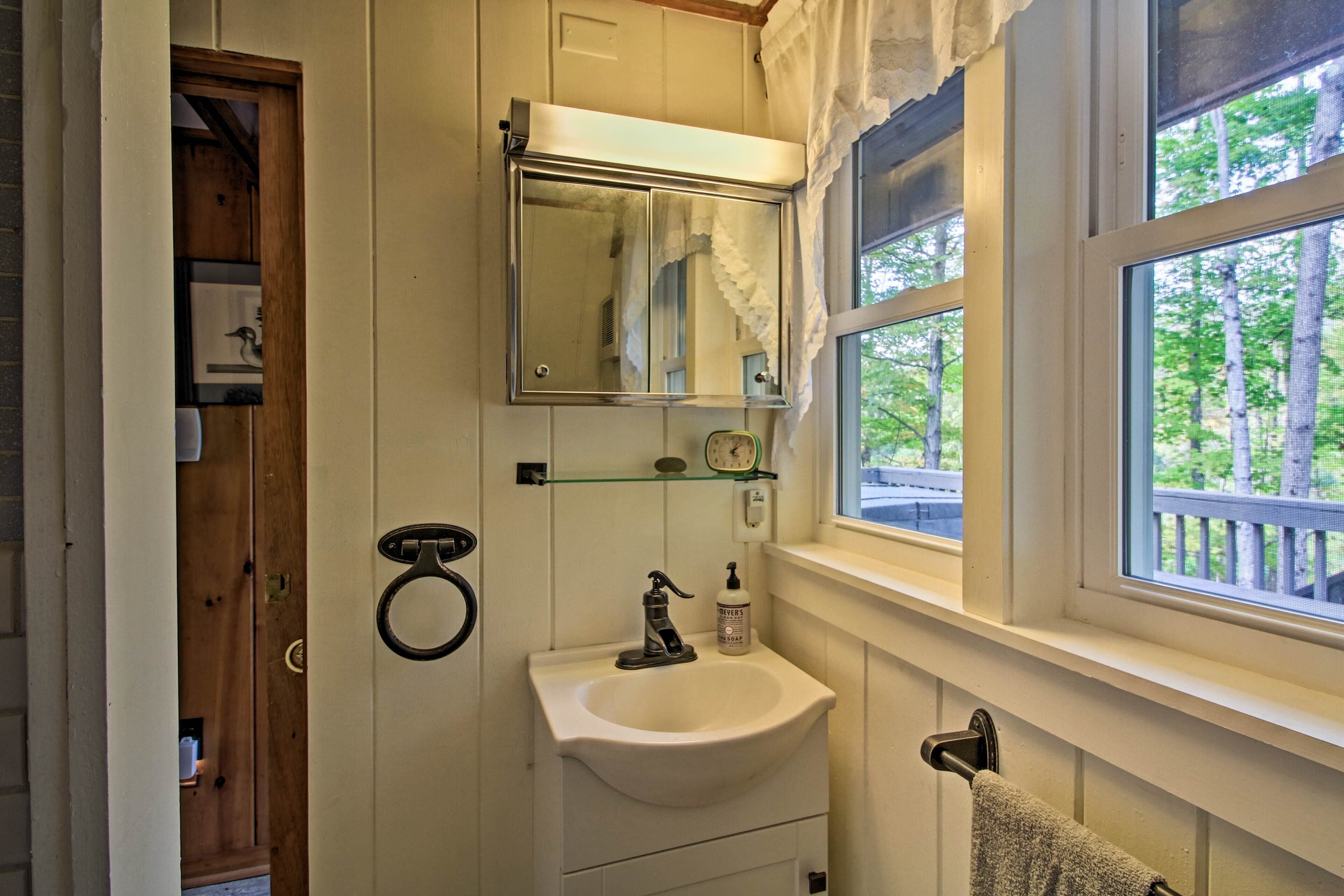 A bathroom with a white sink, a mirror above it, and a window with a view of trees.