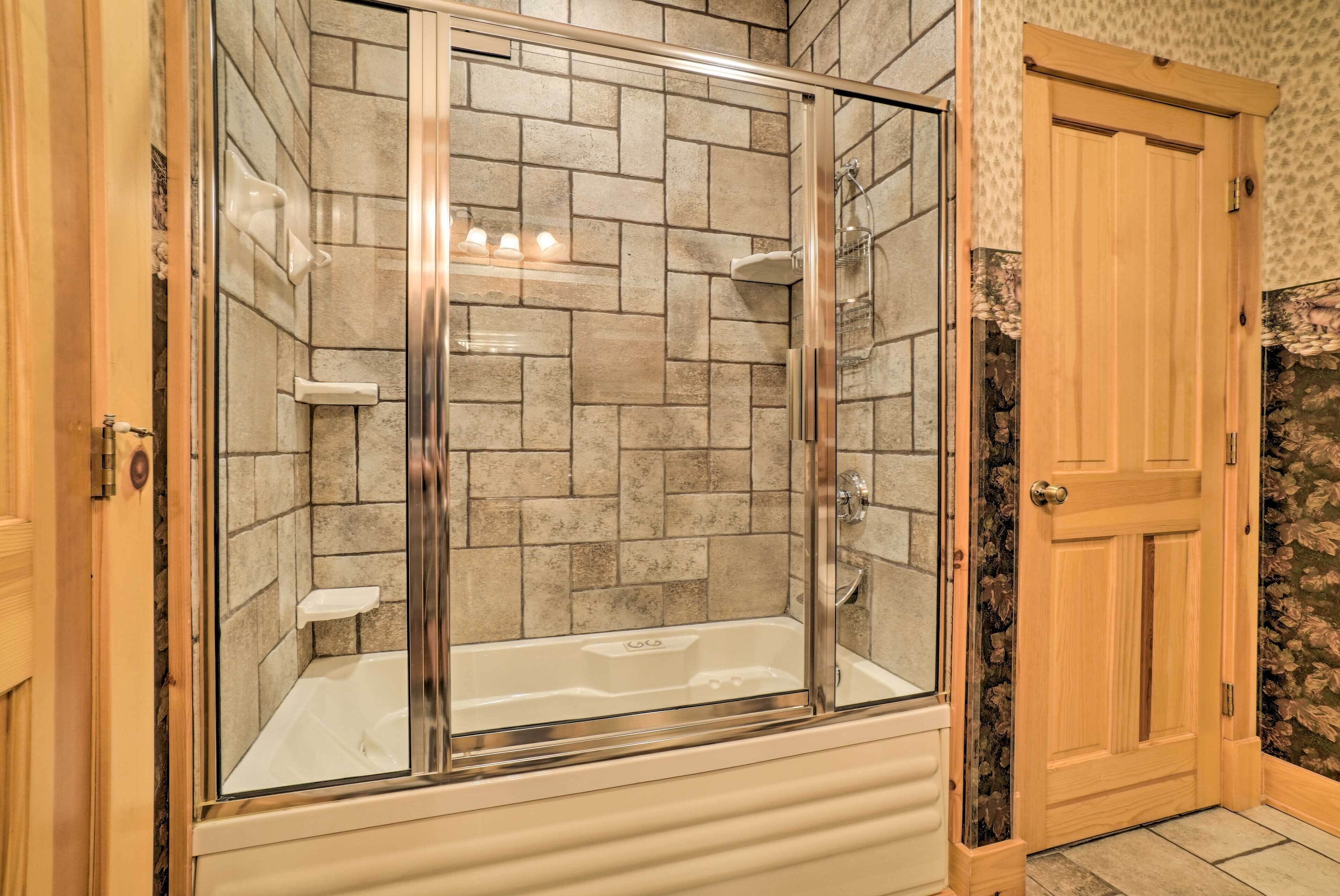 A glass-enclosed shower area with a bathtub, tiled walls, and a wooden door.