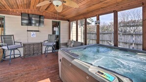 A covered outdoor area with a hot tub, wooden ceiling, and seating.