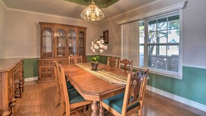 A dining room with a wooden table, chairs, a chandelier, and a large window.