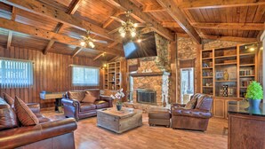 A spacious living room with leather sofas, a stone fireplace, wooden ceiling beams, and built-in bookshelves.