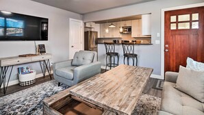 A modern living room with a wooden coffee table, a grey sofa, and a TV mounted on the wall. - Home: Grassy Yard, Walk to Bentonville Square (Bentonville)