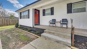 A single-story house with a red door, two windows with shutters, and a small porch with two chairs. - Home: Grassy Yard, Walk to Bentonville Square (Bentonville)