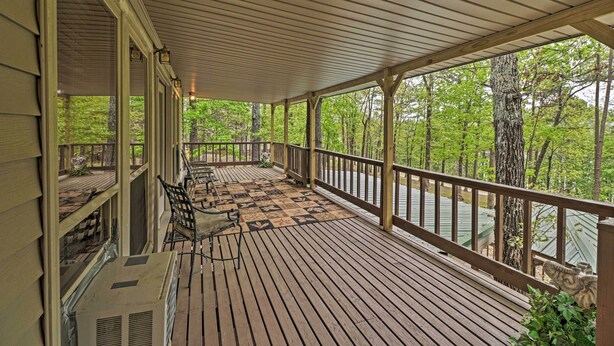 A covered wooden deck with a railing, benches, and a view of a forest.