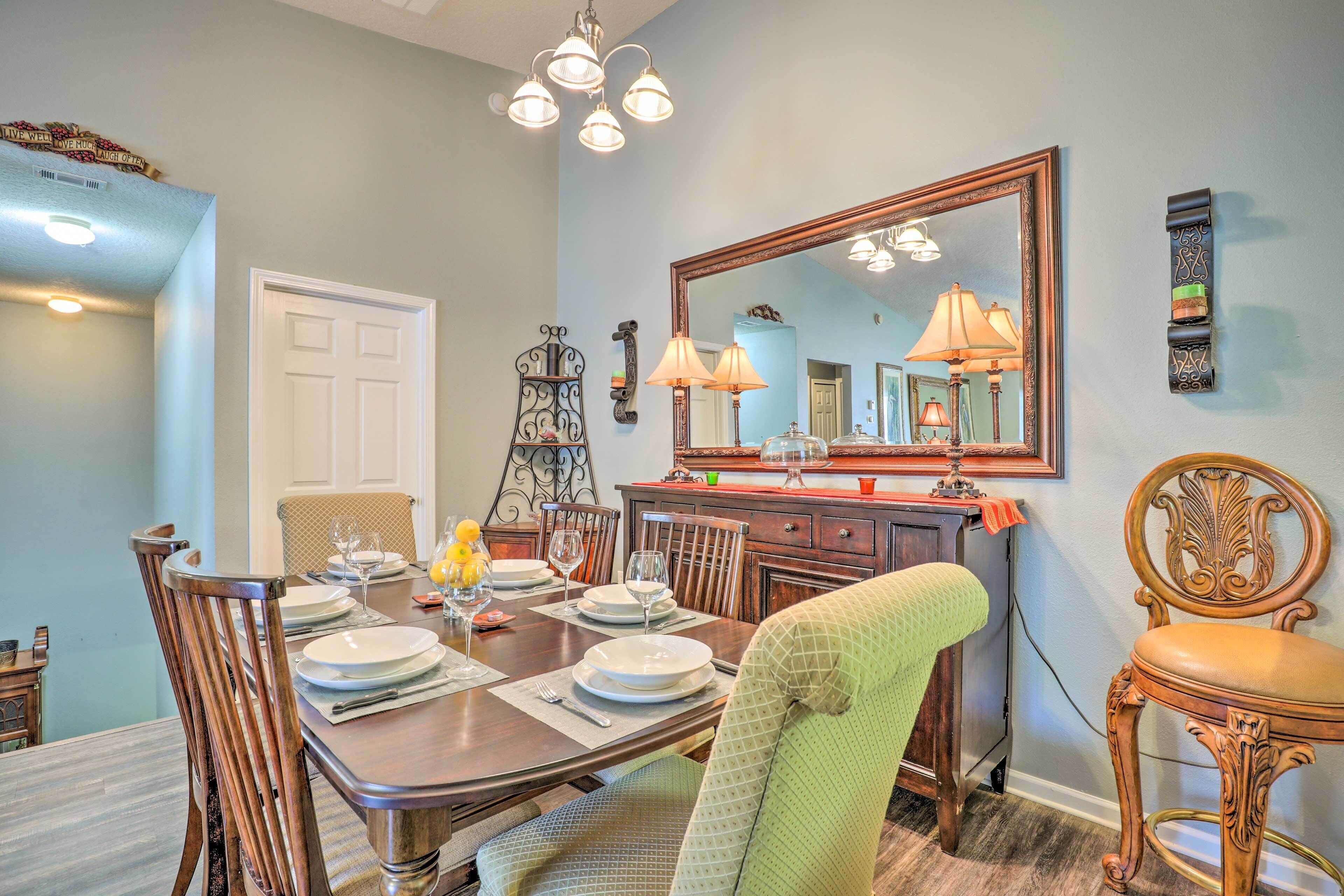 A dining room with a wooden table set for four, a large mirror, and a chandelier.