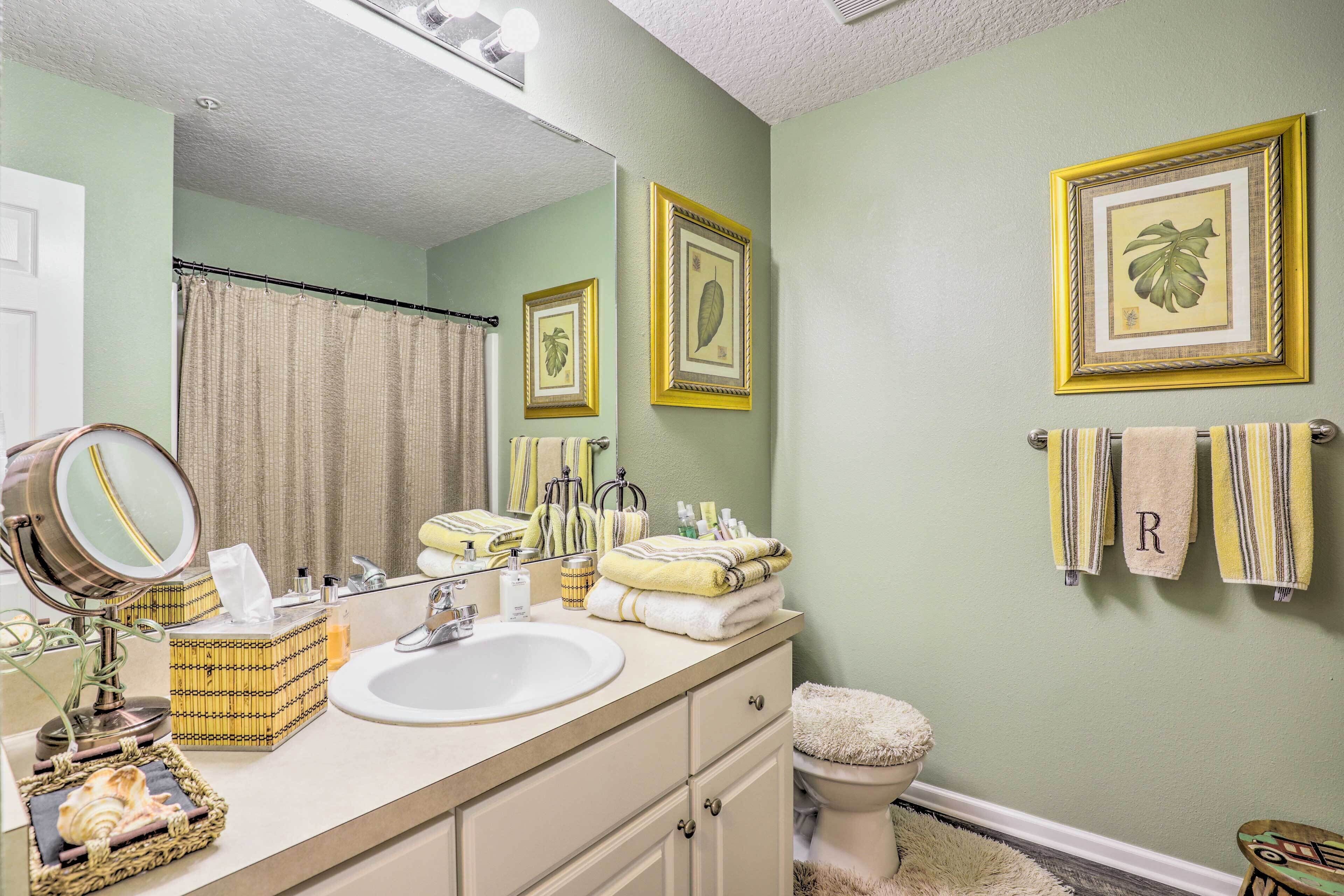 A bathroom with a sink, mirror, and toilet. There are towels and toiletries on the counter.
