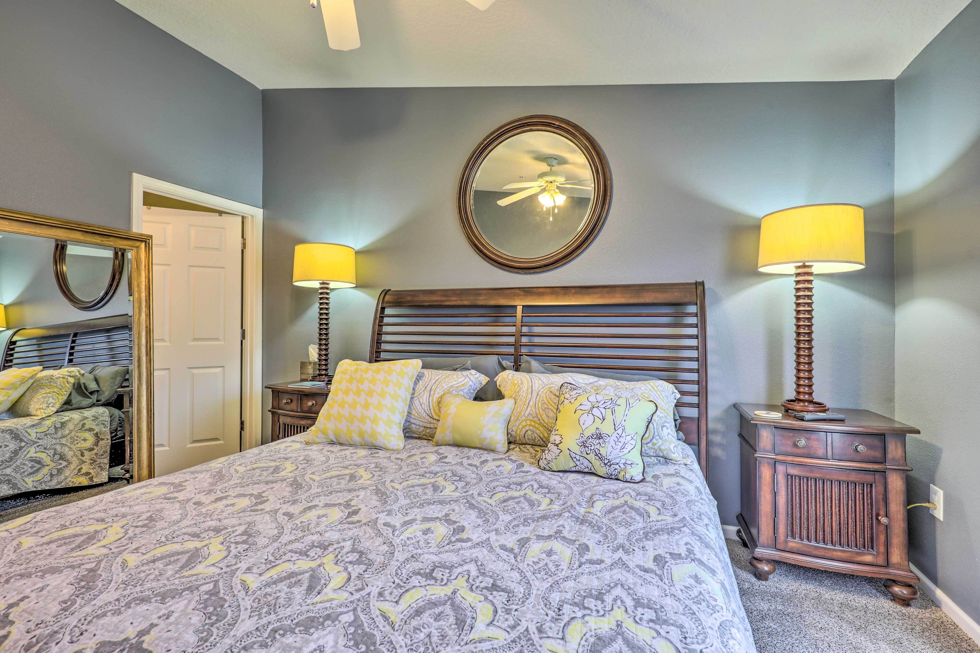 A bedroom with a bed, two bedside tables with lamps, a mirror, and a ceiling fan.