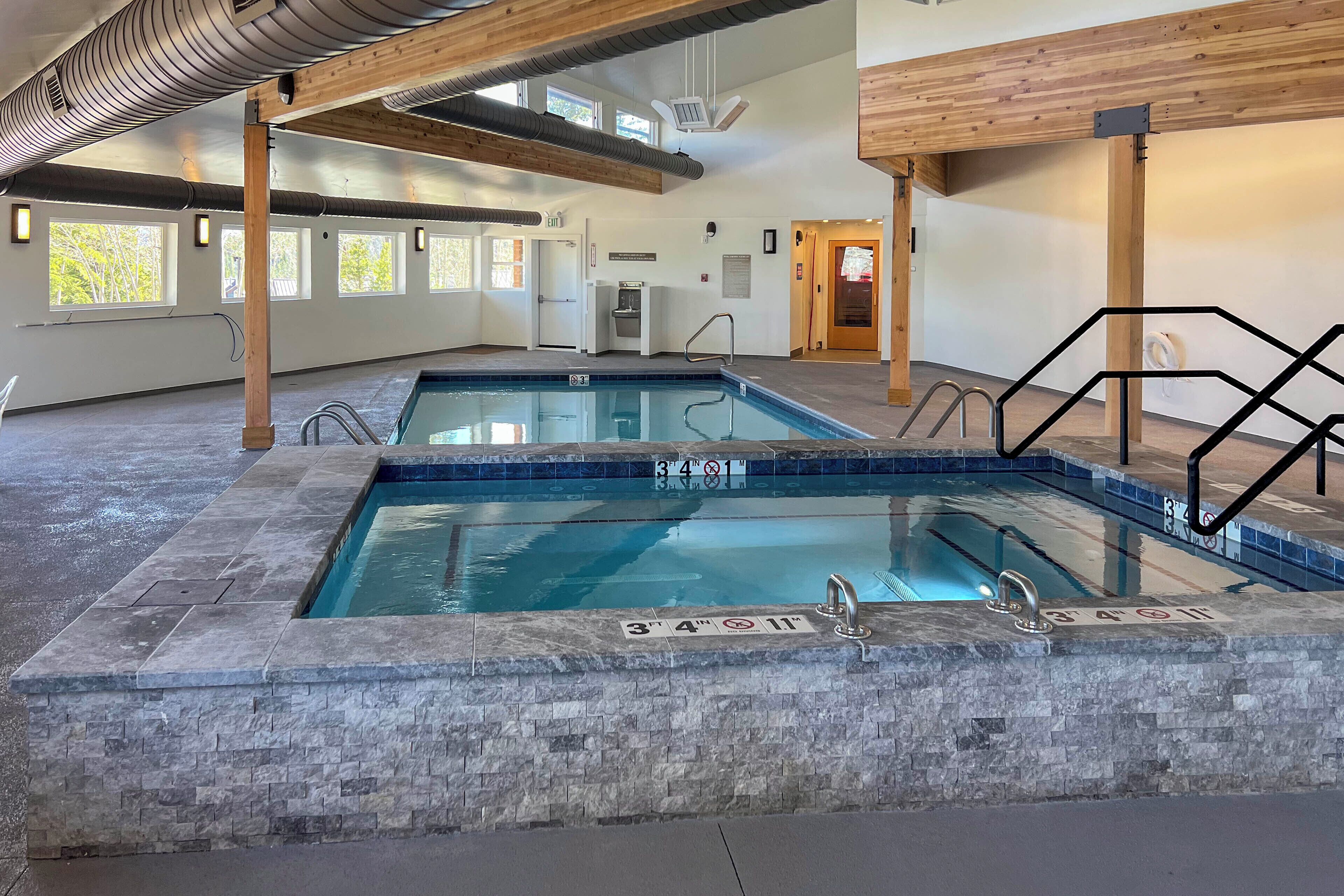 An indoor swimming pool with clear water, a stone border, and a metal ladder.