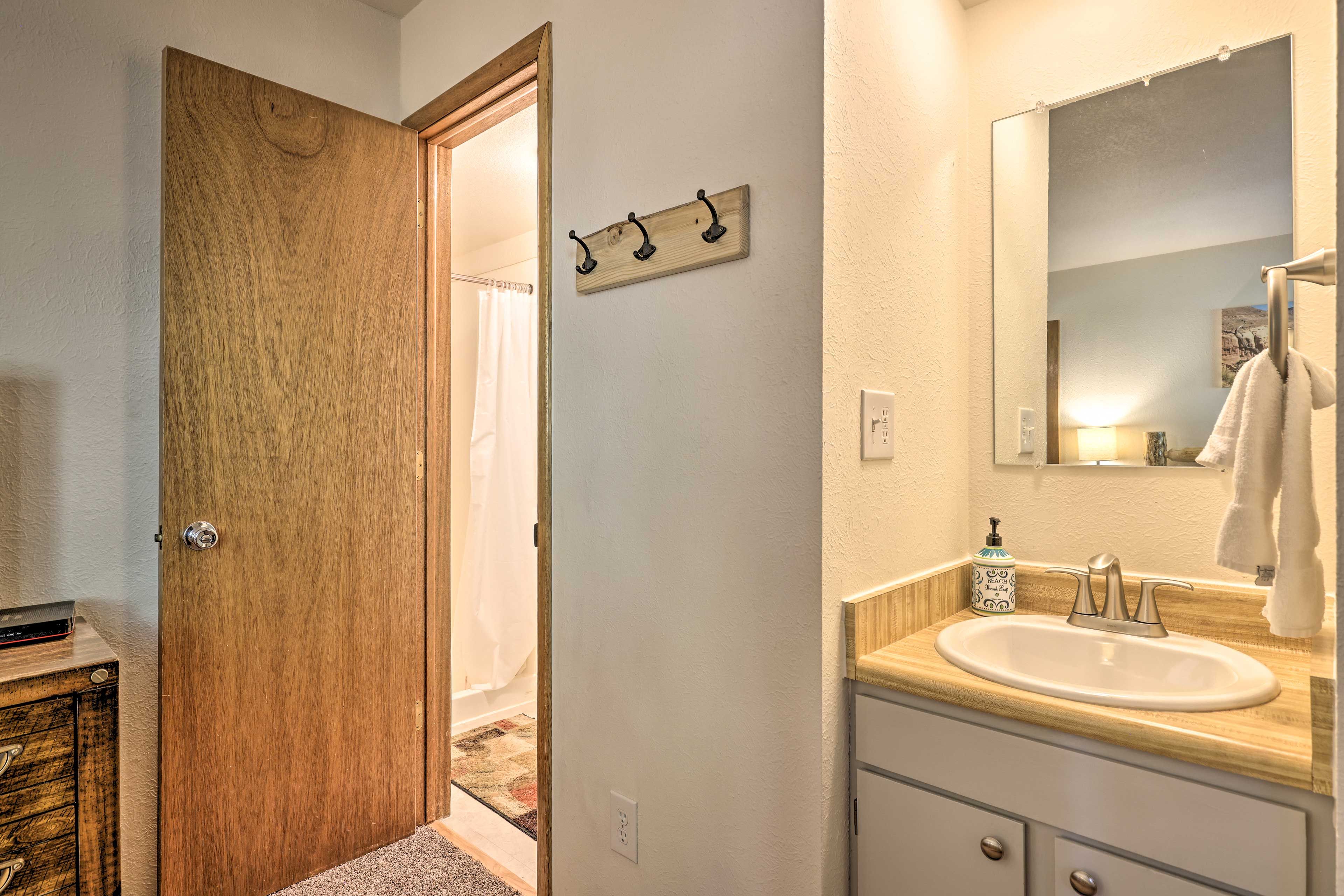 A bathroom with a wooden door, a sink with a mirror, and a towel hanging on the wall.