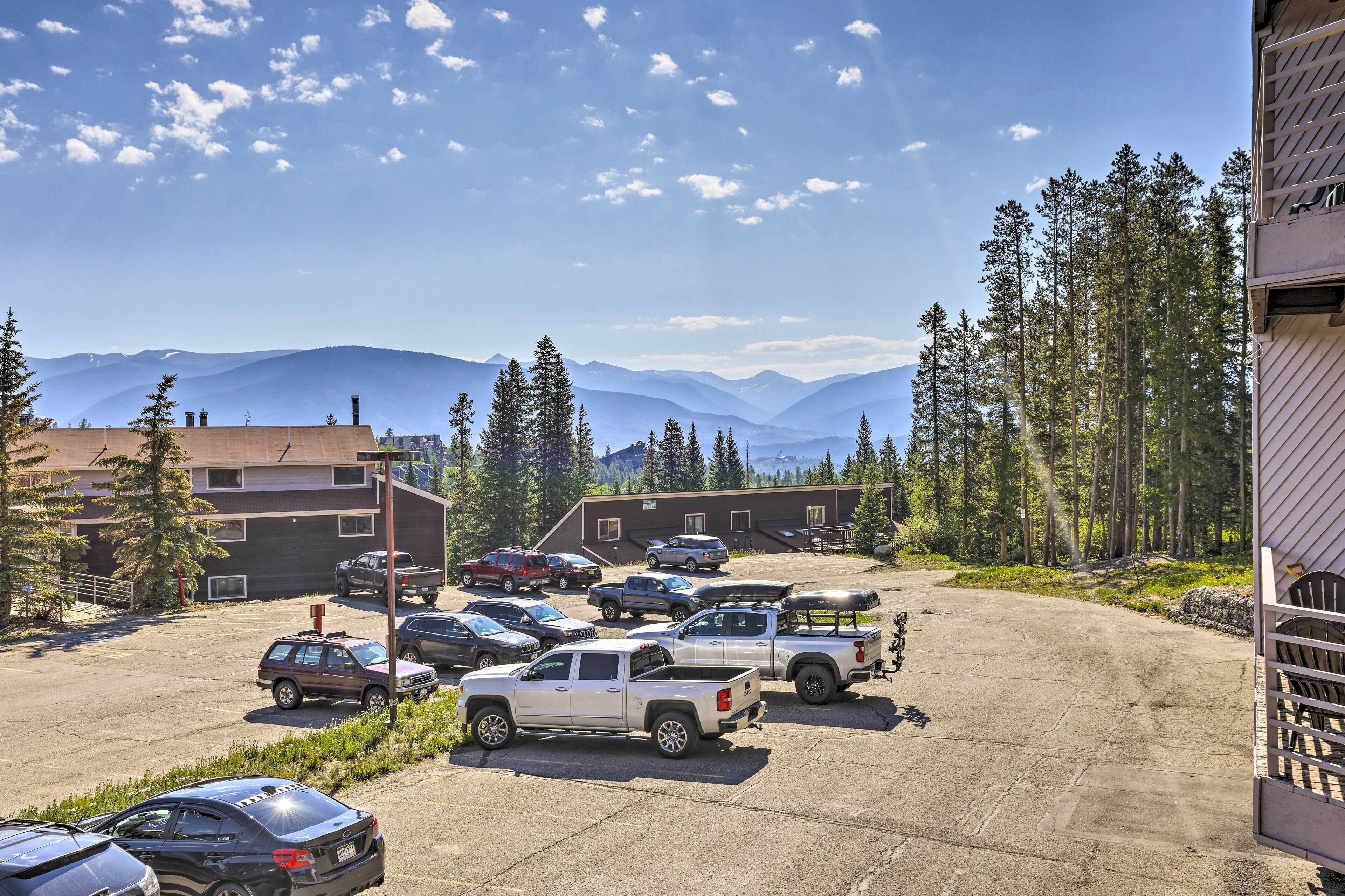 A parking lot with several vehicles, a building with a sloped roof, and a mountainous backdrop.