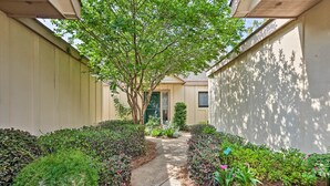 A narrow pathway flanked by lush greenery and a large tree providing shade.