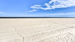 A wide, sandy beach with footprints leading towards the ocean under a clear blue sky.