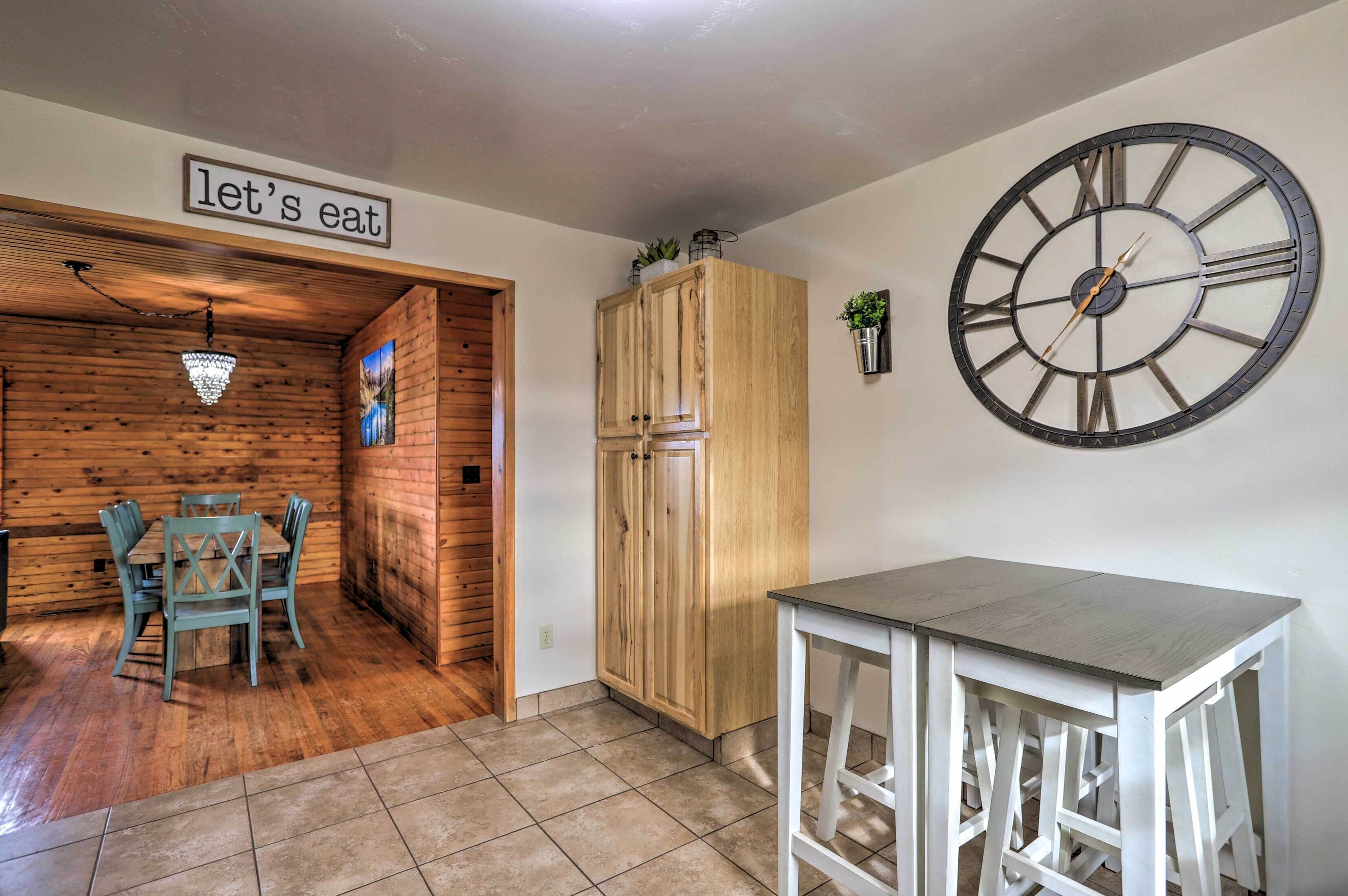 Un coin repas avec une table et des chaises en bois, une grande horloge murale et un panneau sur lequel on peut lire : « à table ! »