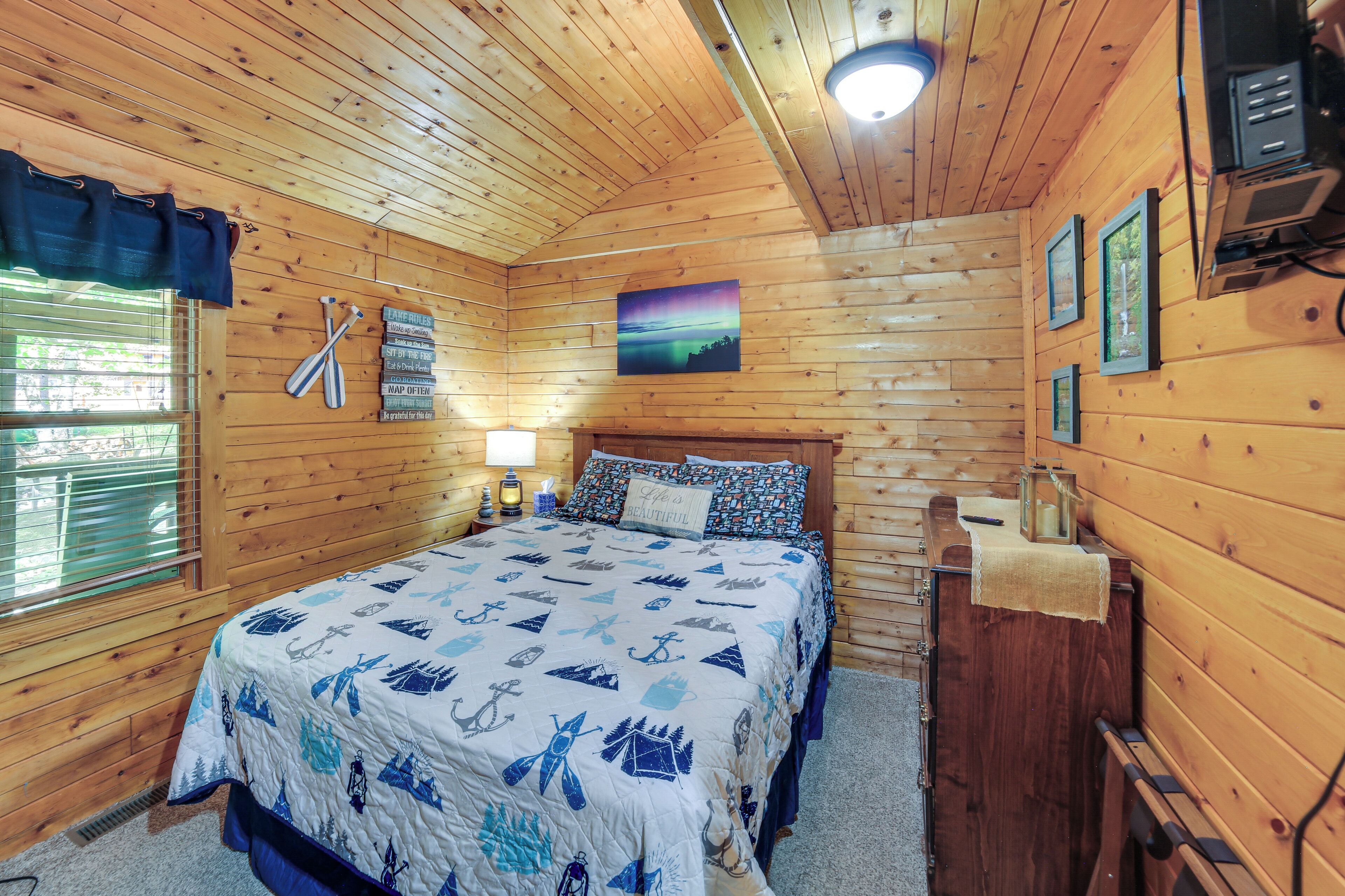 Un dormitorio de cabaña de madera con cama, mesita de noche, lámpara y un cuadro en la pared.