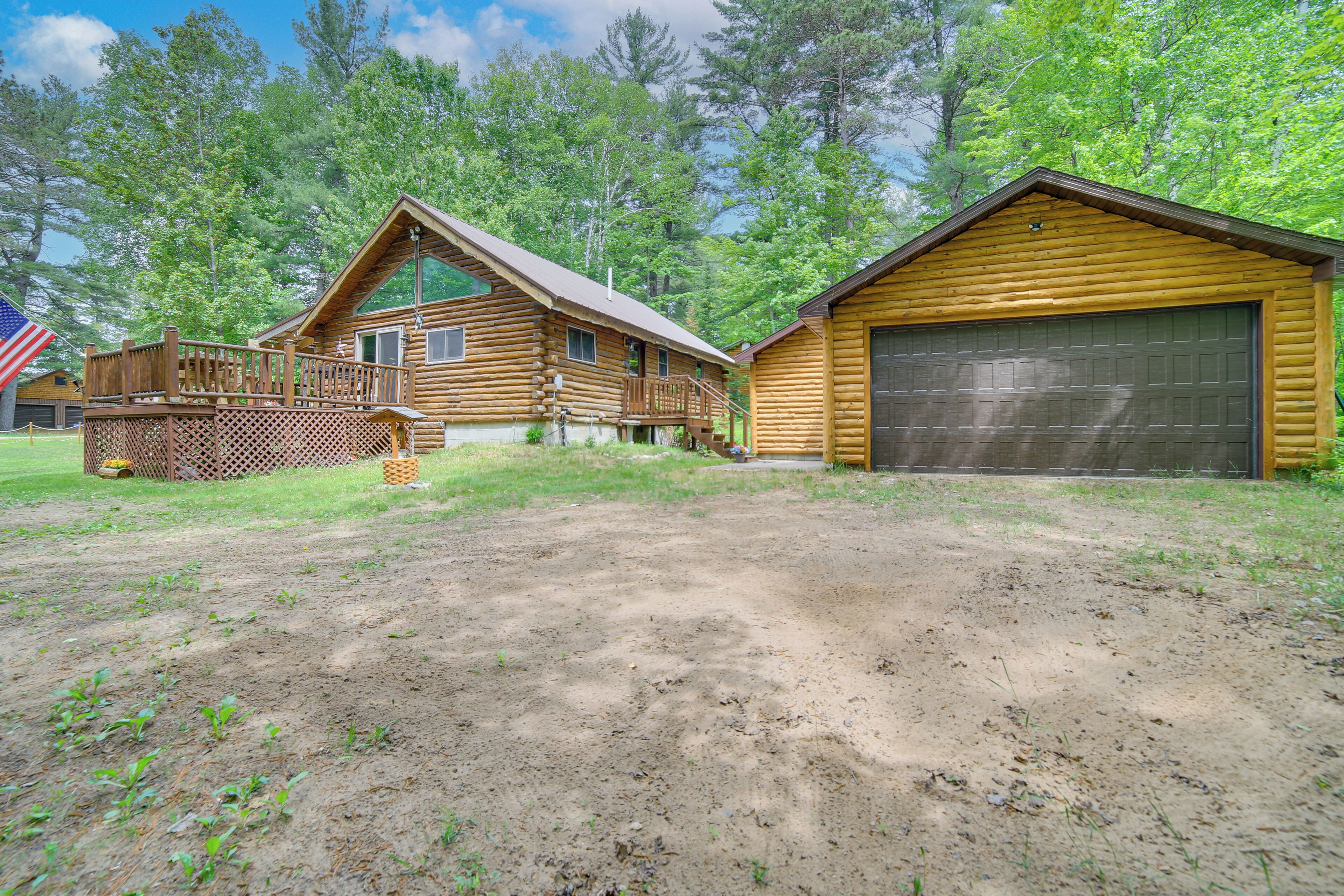 A wooden cabin with a deck, a garage, and a fenced area with a flag.