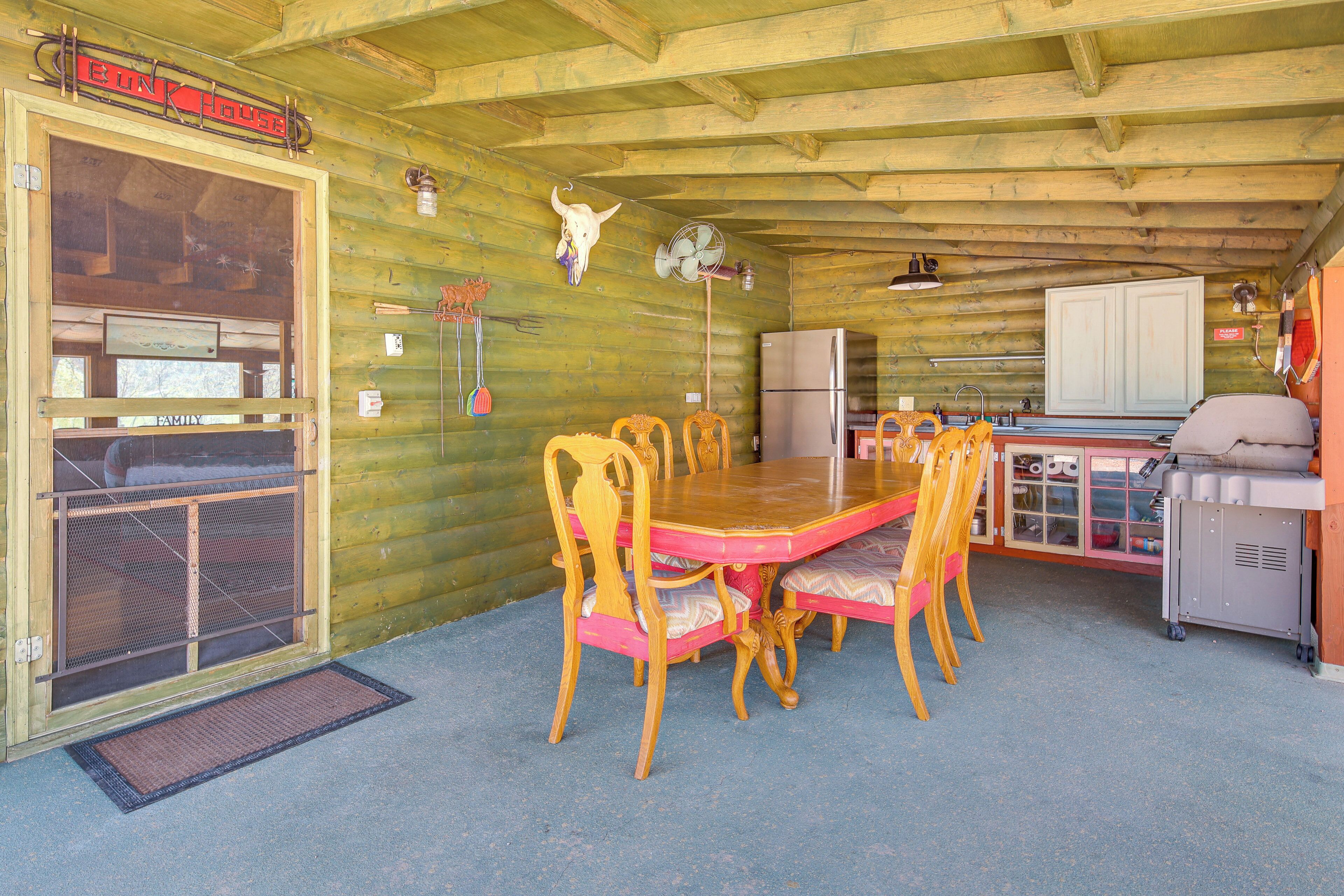 Een houten blokhut van binnen met een eettafel, stoelen, een koelkast en een grill.