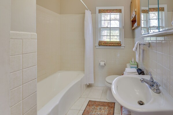 Un baño con bañera, inodoro, lavabo y ventana con cortina.