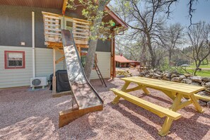 A wooden deck with a slide, picnic tables, and a building with a red roof.