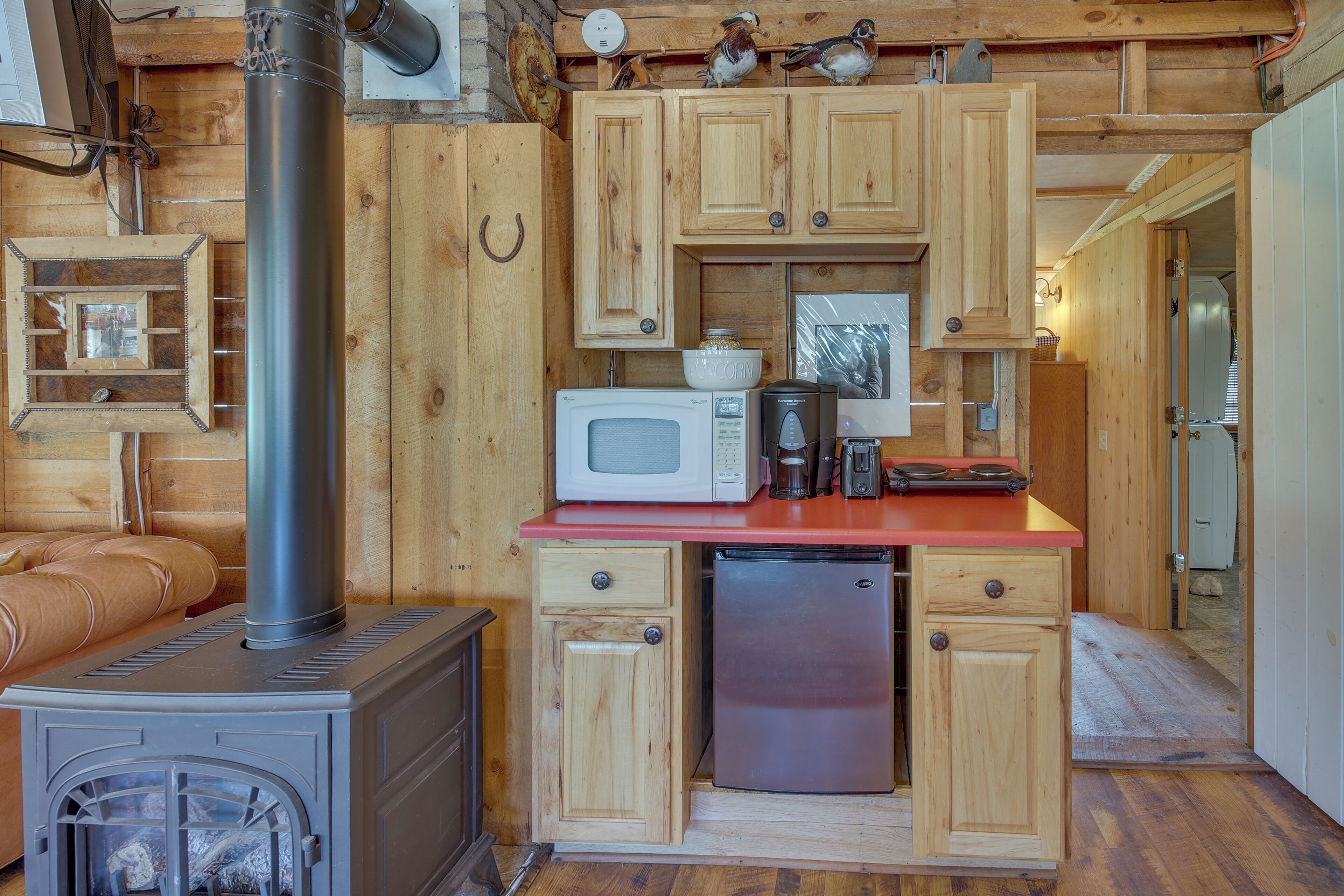 Una cocina compacta con armarios de madera, microondas, cafetera y cocina empotrada.