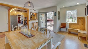 A spacious living area with a wooden dining table, white chairs, and a bench. There is a kitchen visible through an open door, and a large window with a view of the outdoors. - The Ranch at Keystone: 9 Mi to Mount Rushmore! (Keystone)