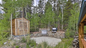 En stuga byggd av trä med en steneldstad och ett grillområde, omgiven av en vacker, naturlig skogsmiljö.