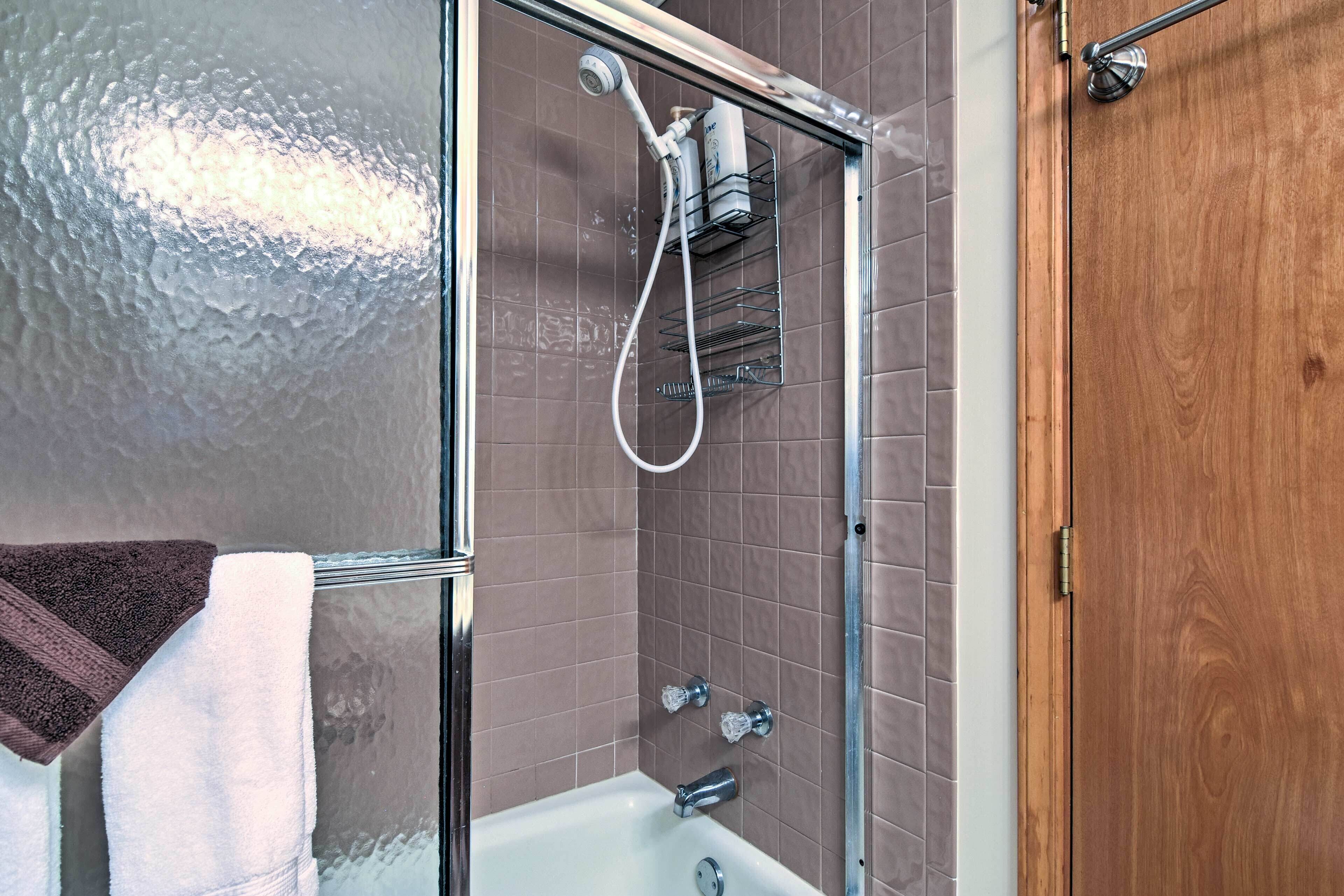 A bathroom with a glass-enclosed shower, a white bathtub, and a wooden door.