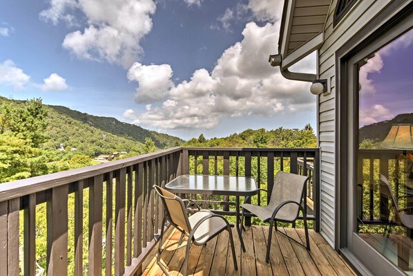 A wooden deck with a glass table and chairs, overlooking a mountainous landscape.