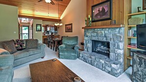 A cozy living room with a stone fireplace, a sofa, a coffee table, and a television on a wooden stand. - Year-round Fun in Beech Mountain! Condo w/ Balcony (Banner Elk)