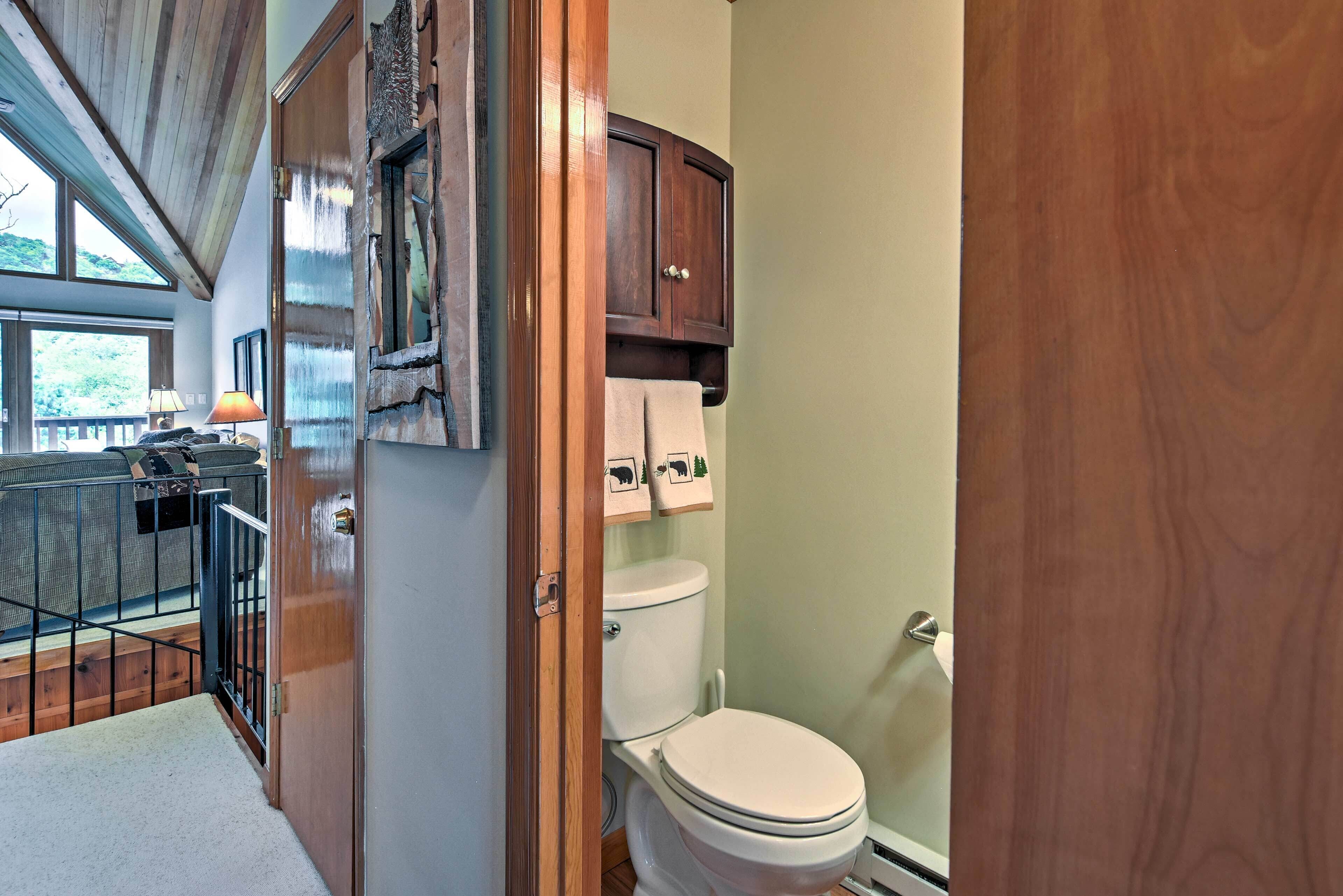 Une petite salle de bain comprenant des toilettes, un meuble en bois placé au-dessus et une fenêtre laissant entrer la lumière naturelle.