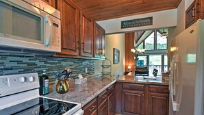 A kitchen with wooden cabinets, a microwave, stove, and a sign that reads "Welcome to The Mountains". - Year-round Fun in Beech Mountain! Condo w/ Balcony (Banner Elk)