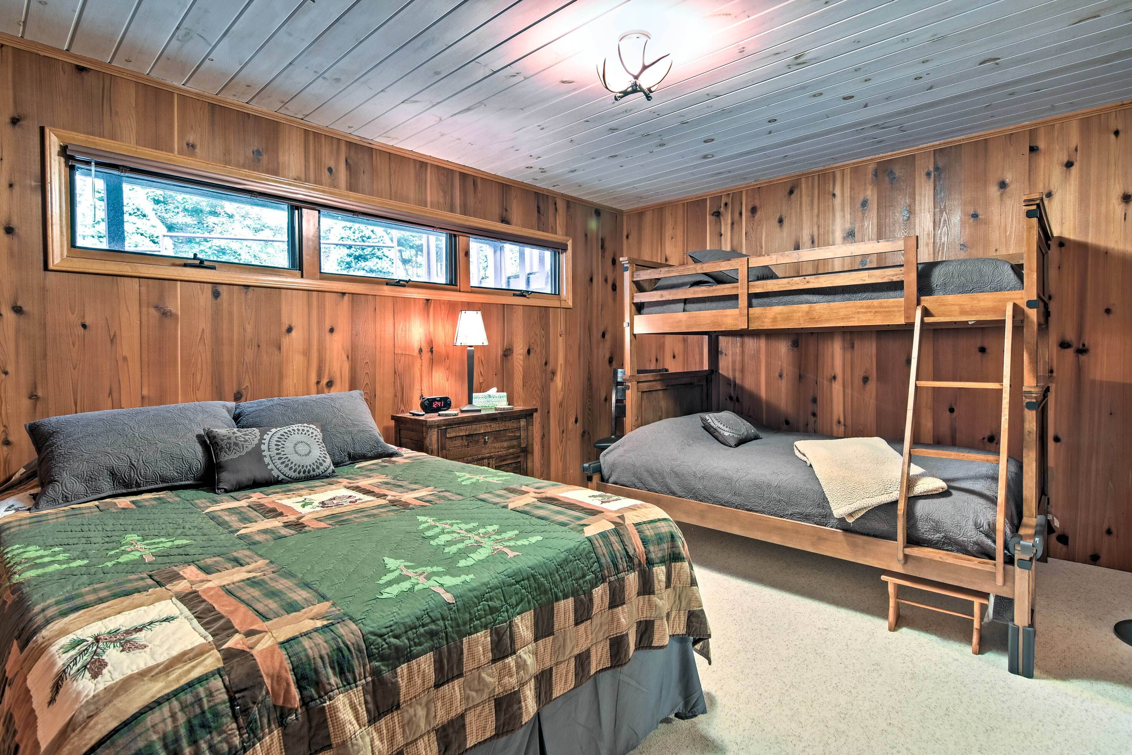 Ein Zimmer mit einem Etagenbett, einem großen Bett mit Patchworkdecke, Holzwänden, einem Fenster und einer Lampe.