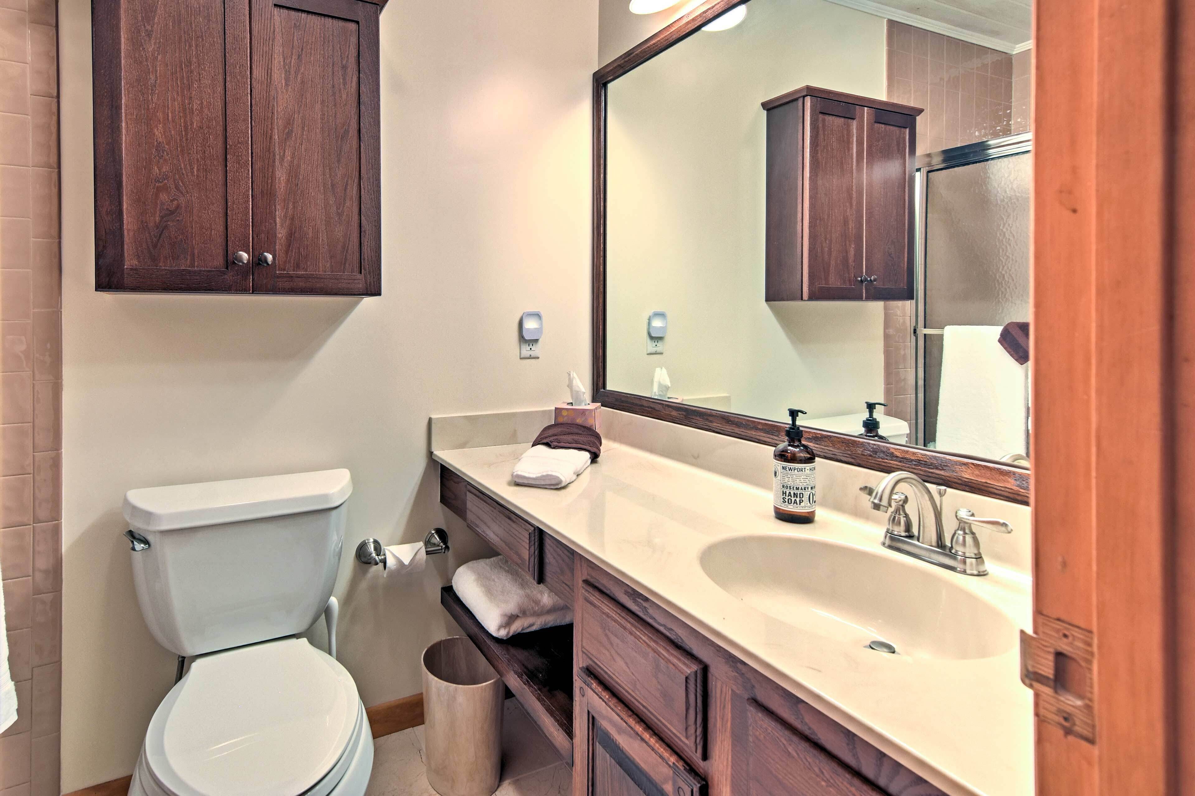 A bathroom with a toilet, sink, mirror, and wooden cabinets.