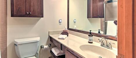 A bathroom with a toilet, sink, mirror, and wooden cabinets.