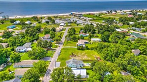 An aerial view of a residential area with houses, green lawns, and a beach in the background. - Charming Coastal Getaway, Near Beach & Pier! (Gulfport)