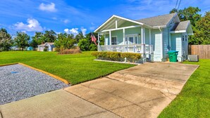 A light blue house with a porch, a front yard with a gravel area, and a wooden fence. - Charming Coastal Getaway, Near Beach & Pier! (Gulfport)