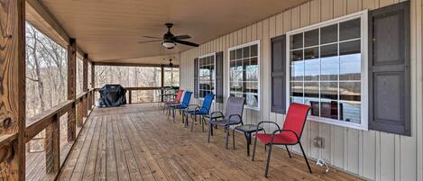 A covered porch with wooden flooring, a ceiling fan, and a row of chairs.