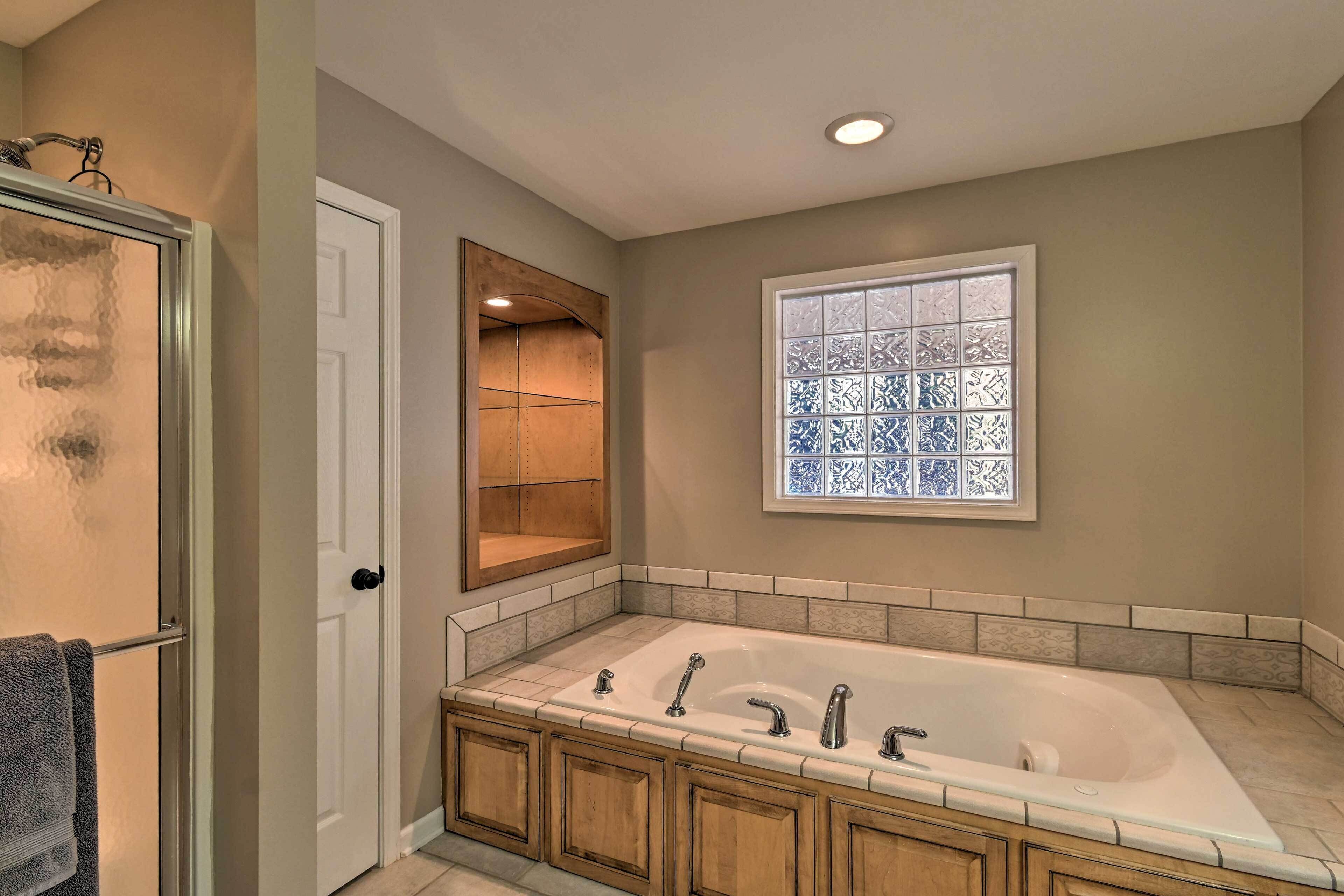 Une salle de bain dotée d’une grande baignoire, de meubles en bois, d’une cabine de douche en verre et d’une fenêtre décorative.