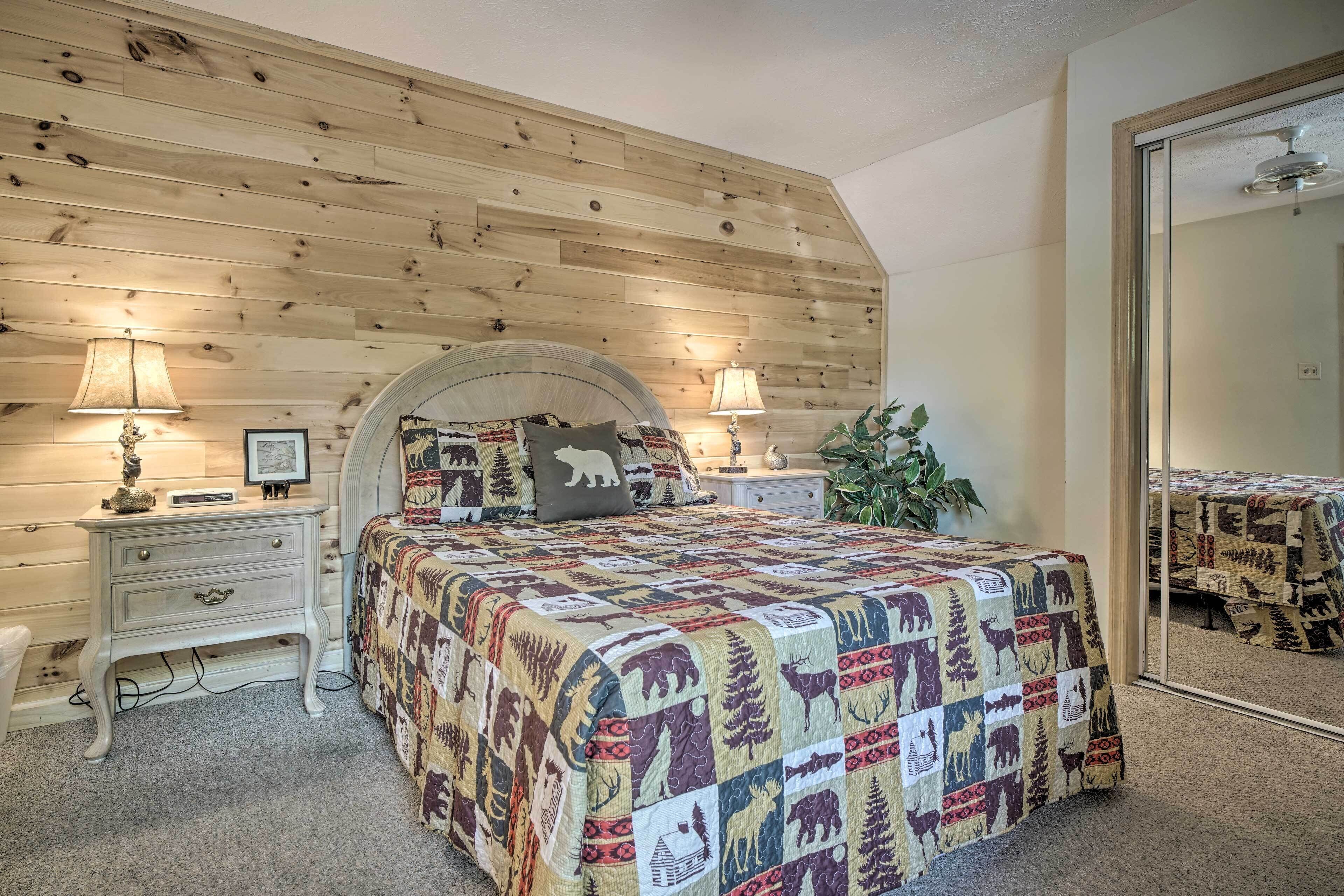 A bedroom with a wooden slat ceiling, a bed with a quilted blanket, two bedside tables with lamps, and a large mirror on the wall.