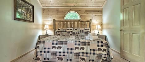 A bedroom with a checkered bedspread, a wooden ceiling, a window, and a door.