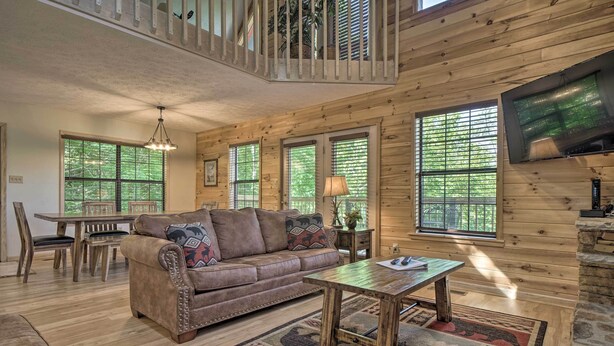 A spacious living room with a wooden floor, a brown leather sofa, a coffee table, and a TV mounted on the wall. - Hot Tub & Private Deck: Rustic Pigeon Forge Cabin (Pigeon Forge)