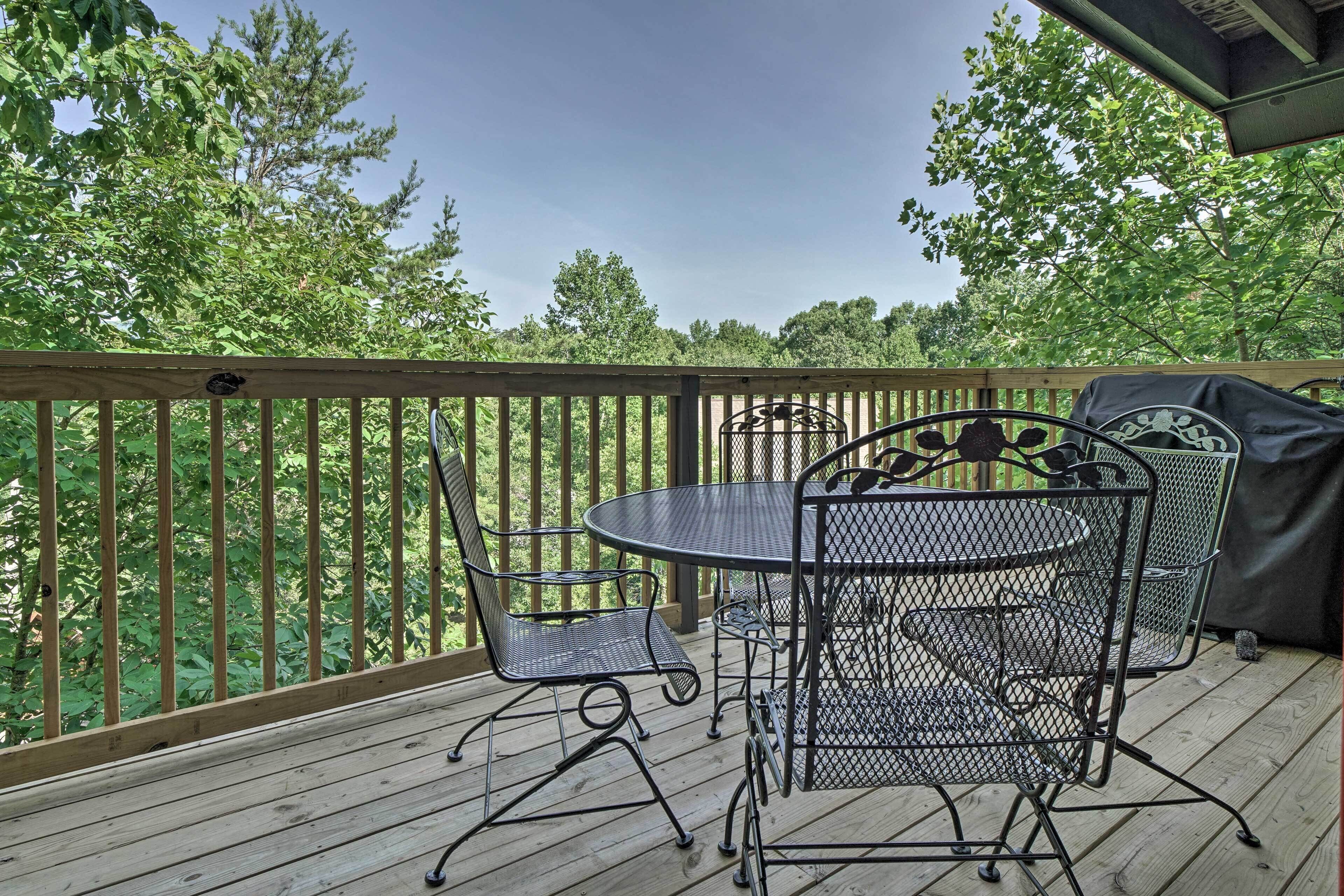 A wooden deck with a metal table and chairs, surrounded by a wooden railing and trees.