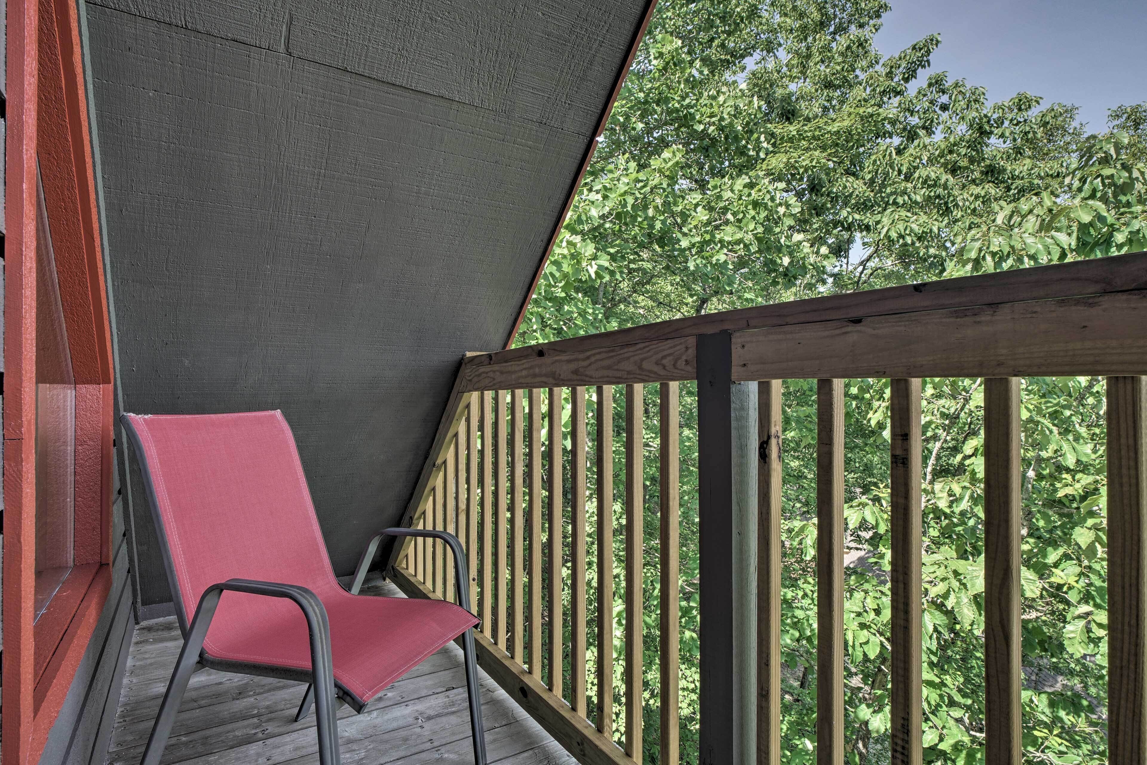 Une terrasse en bois avec une chaise rouge, une rambarde en bois et une vue sur les arbres.