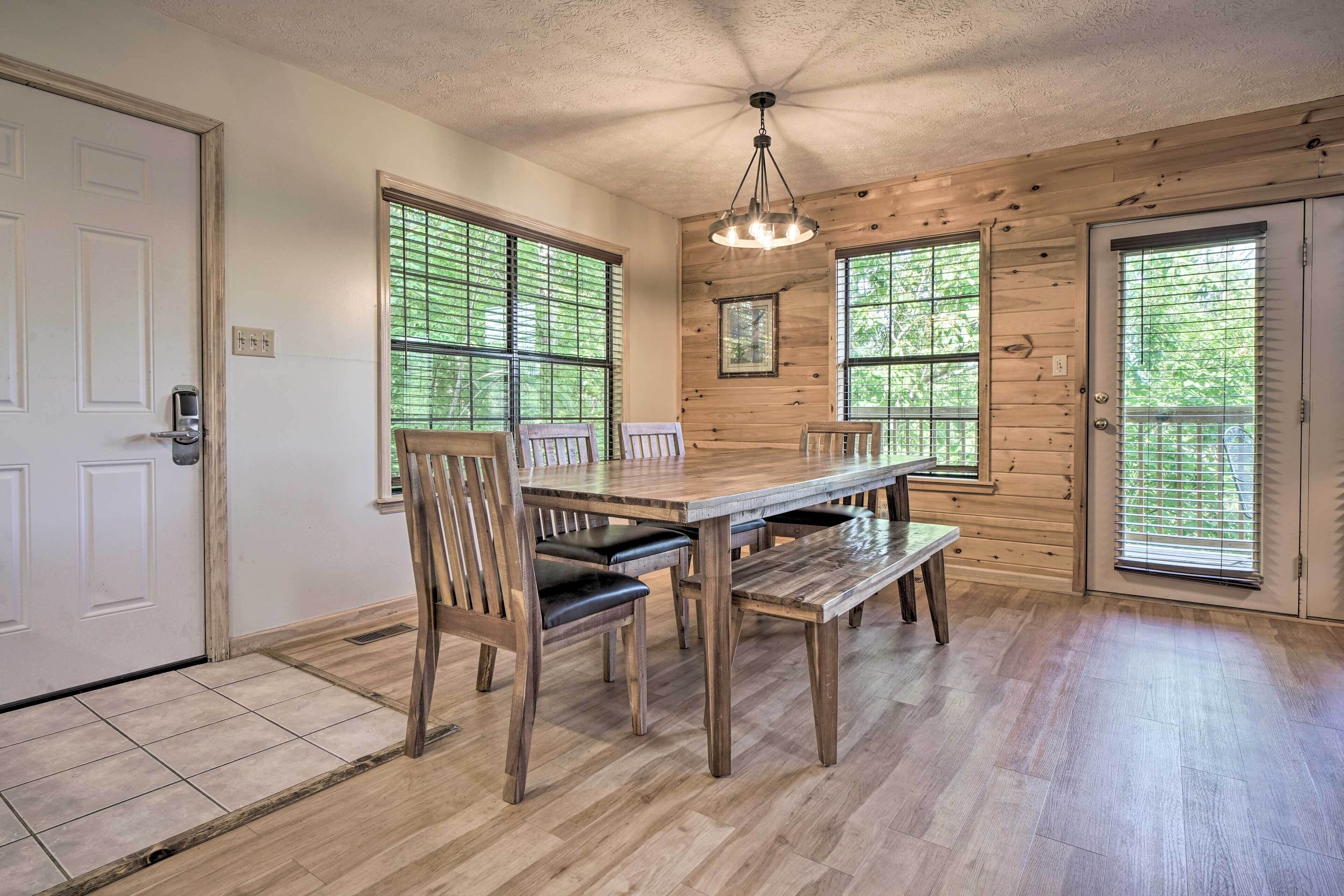 A dining area with a wooden table and chairs, large windows with blinds, and a ceiling fan.