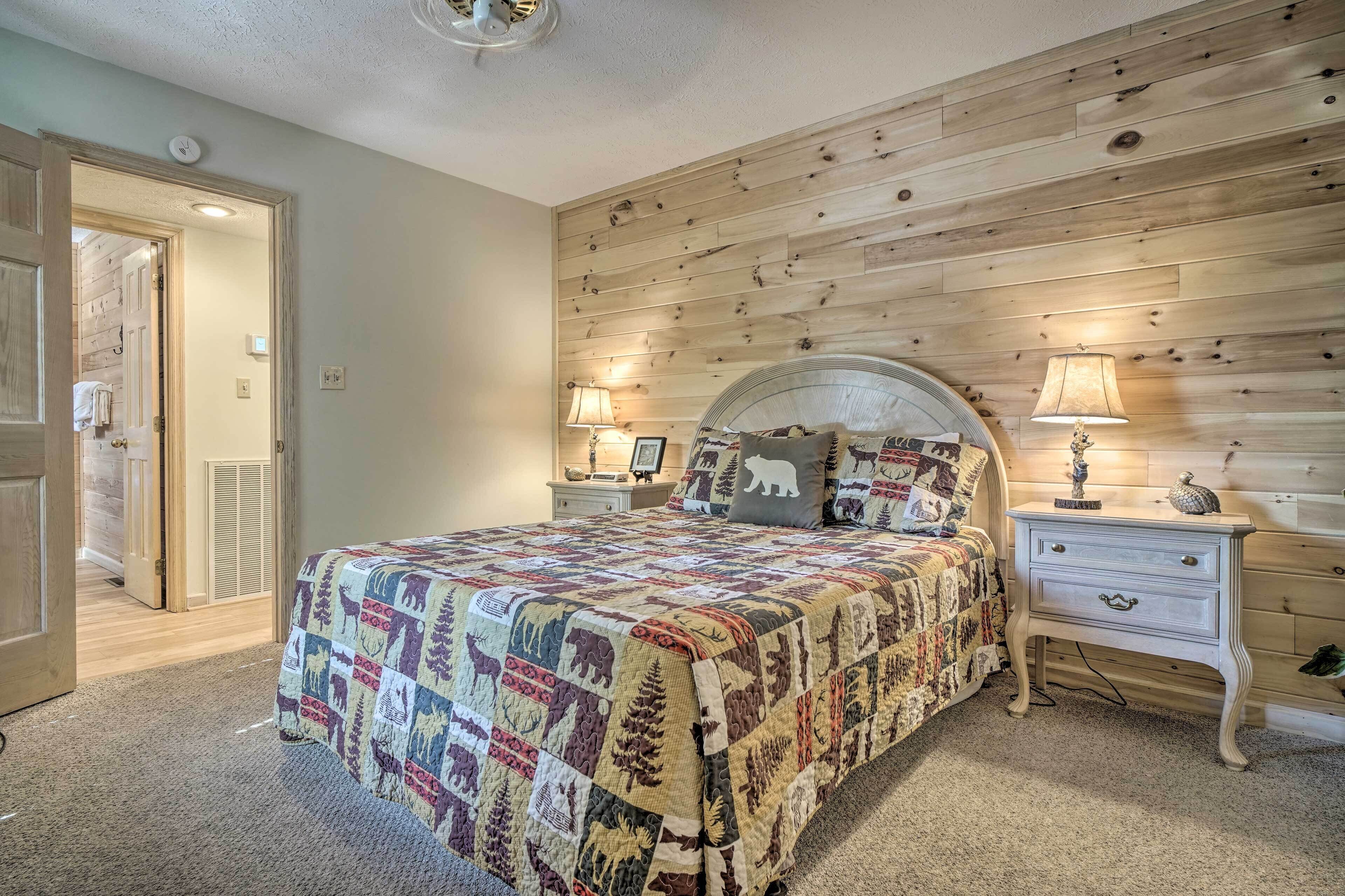 Un dormitorio con pared de paneles de madera, colcha acolchada, mesita de noche con lámpara y puerta que da a otra habitación.