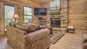 A cozy living room with a stone fireplace, wooden walls, and a large flat-screen TV. - Hot Tub & Private Deck: Rustic Pigeon Forge Cabin (Pigeon Forge)