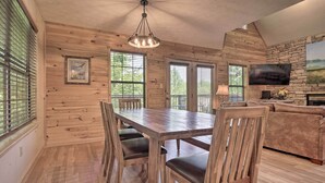 A wooden interior with a dining table, chairs, a sofa, and a TV mounted on a stone wall. - Hot Tub & Private Deck: Rustic Pigeon Forge Cabin (Pigeon Forge)