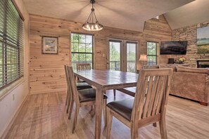 Un interior de madera con una mesa de comedor, sillas, un sofá y un televisor montado en una pared de piedra.