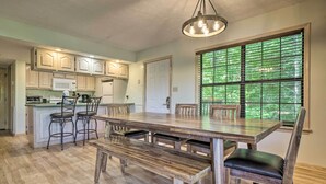 A kitchen with wooden cabinets, a dining table with benches, and a large window with blinds. - Hot Tub & Private Deck: Rustic Pigeon Forge Cabin (Pigeon Forge)