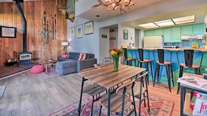 Un salon moderne avec une cheminée, un coin repas avec une table et des chaises en bois, et une cuisine avec des meubles de couleur turquoise.