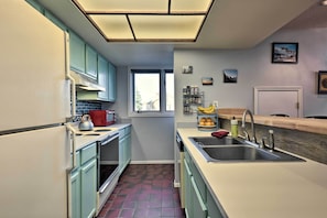 Cozinha compacta com armários verde-água, pia de aço inoxidável e janela que proporciona luz natural.